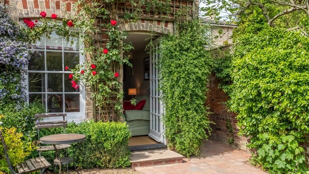 Una casa de ladrillo con entrada al jardín, una pequeña mesa de patio y un banco.