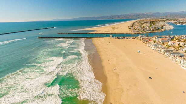 Una playa costera con vista despejada del océano, una orilla arenosa y un puerto deportivo con barcos.