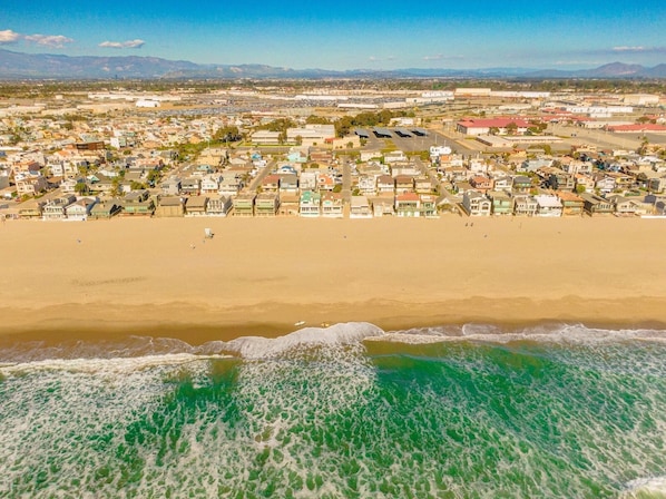 Une vue aérienne d’une ville côtière avec une plage, des maisons et un ciel dégagé.