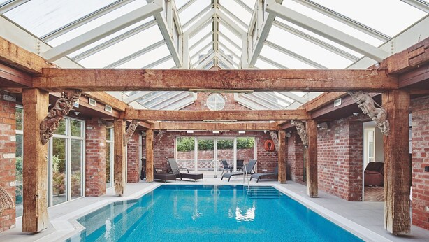 Une piscine intérieure avec un toit en verre, des murs en briques et des chaises longues.
