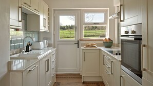 Une cuisine moderne avec des meubles blancs, un four Bosch et une fenêtre donnant sur un champ verdoyant.