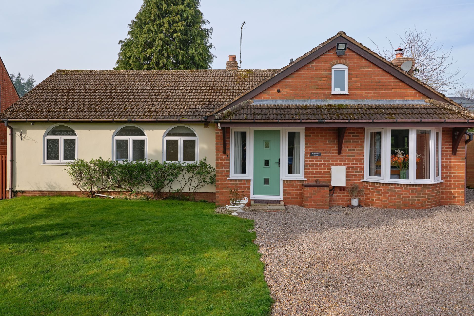 Une maison à deux étages avec une porte verte, un petit porche et une allée gravillonnée.