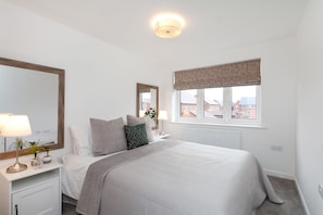 A bedroom with a bed, bedside tables, a mirror, a window with a view, and a ceiling light.