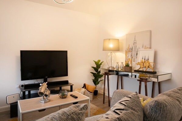 A modern living room with a flat-screen TV, a coffee table, a sofa, a lamp, and a cityscape painting.