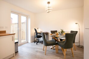 A modern kitchen with a dining area, featuring a table with chairs, a ceiling light, and a view through a sliding door.