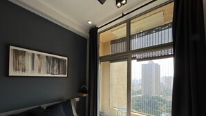 Un dormitorio moderno con una cama grande, vistas de la ciudad a través de una ventana y un cuadro en la pared.