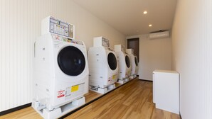 A row of white front-loading washers in a hotel laundry room with wooden flooring and white walls. - HOTEL R9 The Yard Tarui (Tarui)