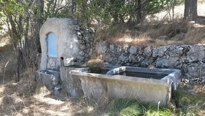 Ein Steingebäude mit einem kleinen Rundbogenfenster und einem rechteckigen Wasserbecken.