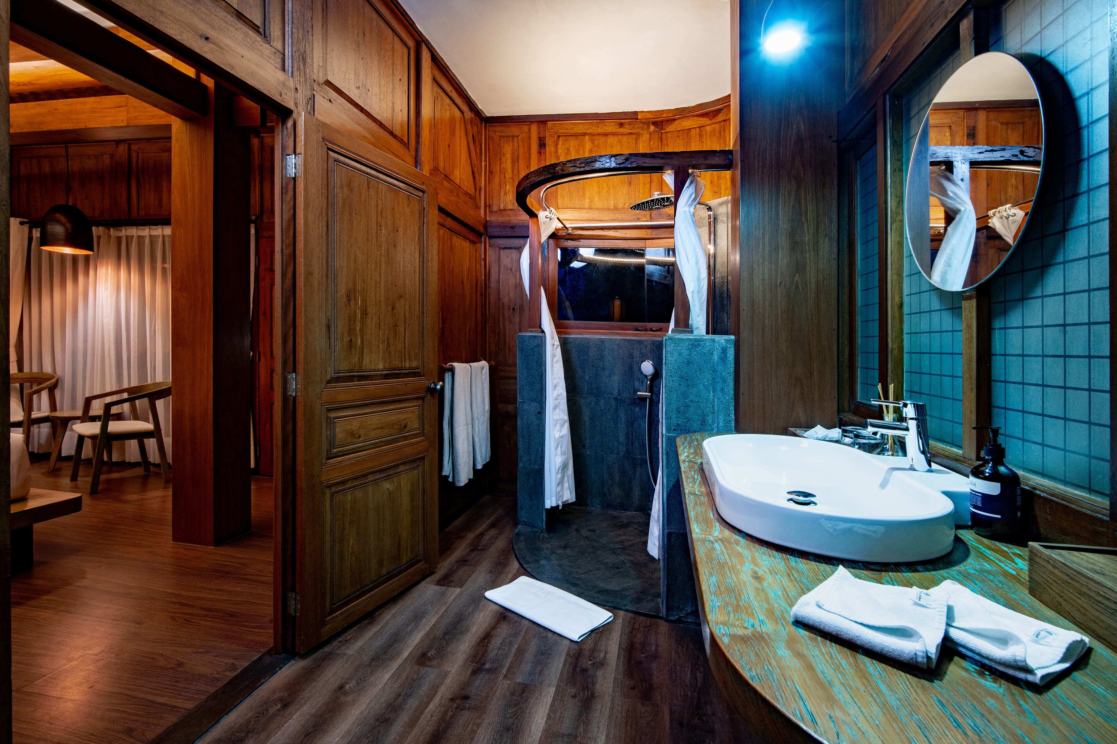 Un baño con detalles de madera, un espejo grande, un lavamanos y una zona de ducha.