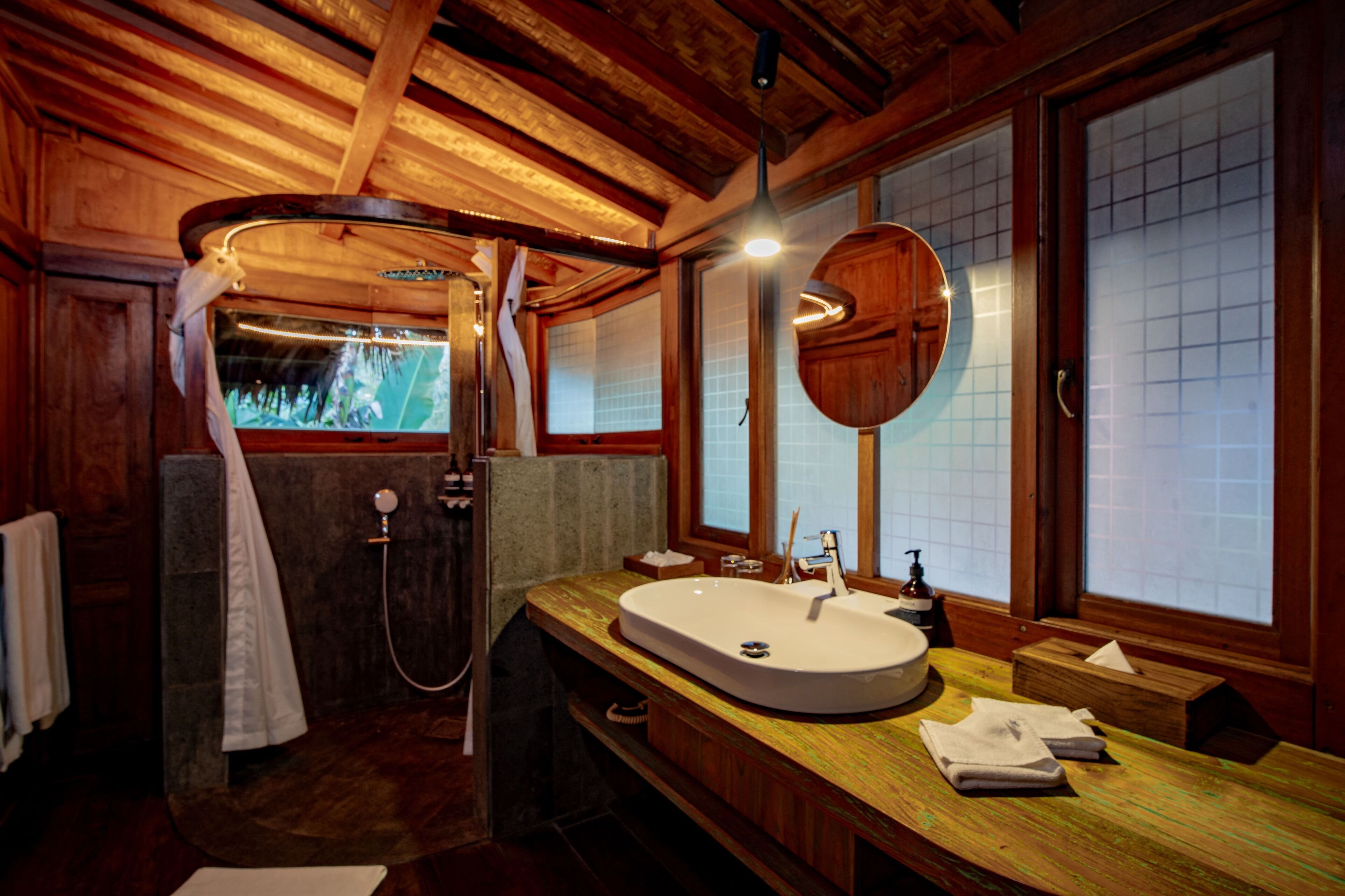 A wooden bathroom with a large sink, a mirror, and a shower.