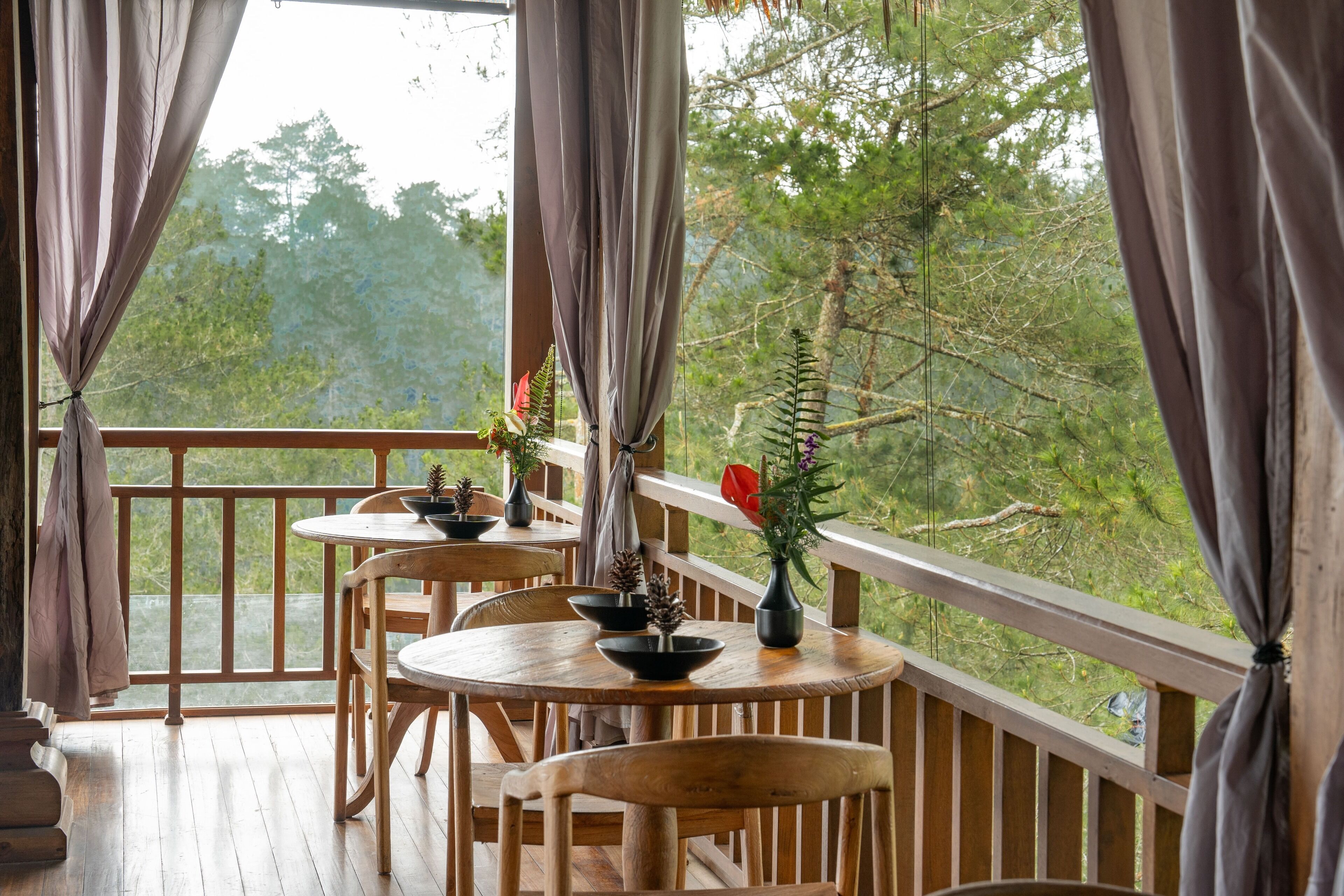 Una terraza de madera con una mesa redonda y sillas, una barandilla y macetas con plantas.