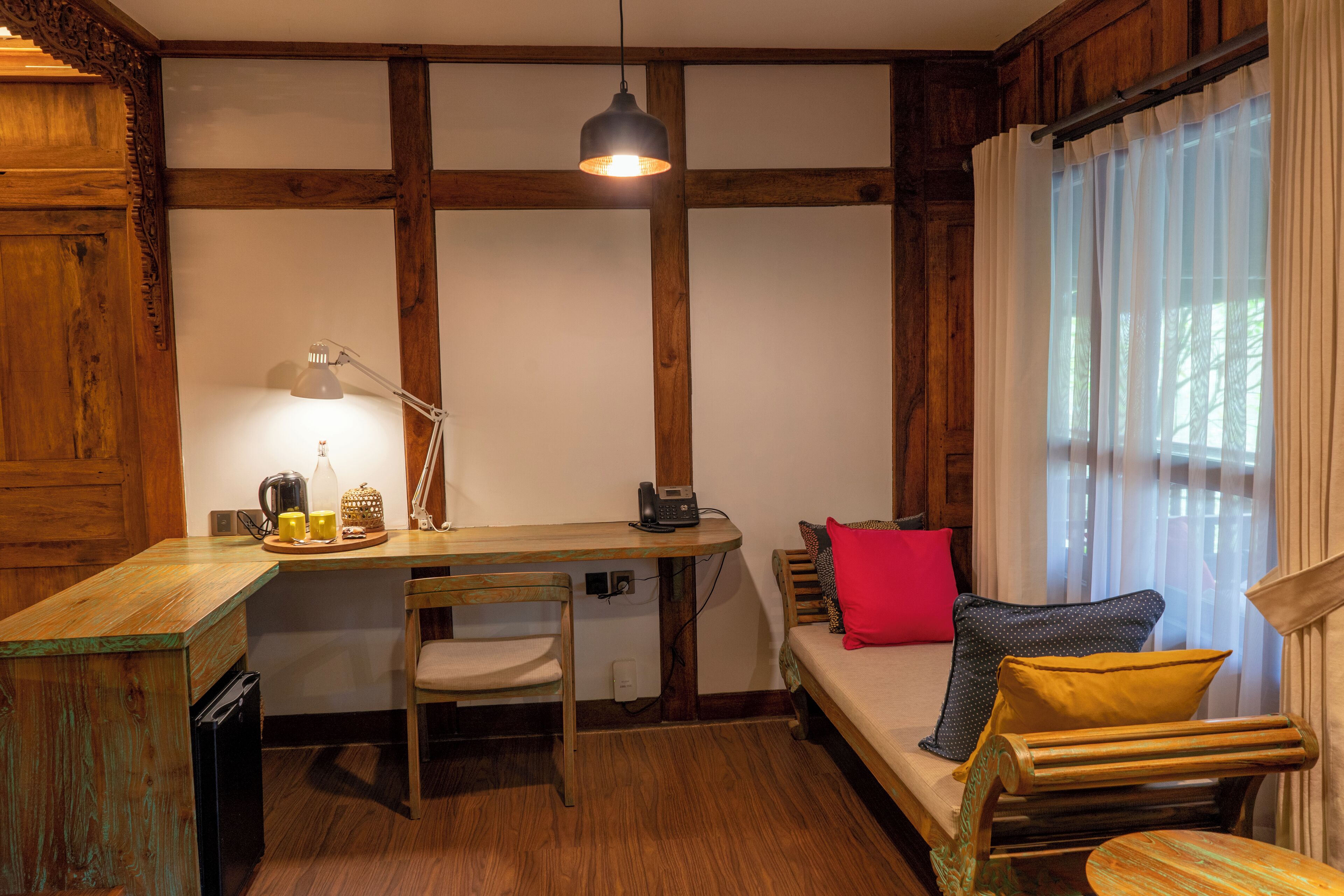 Een gezellige kamer met een houten bureau, een stoel, een bed met kussens en een hanglamp.
