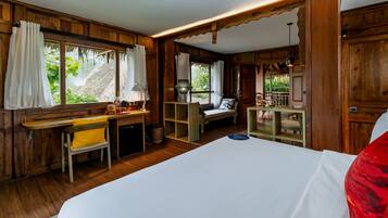 A wooden room with a bed, a desk, and a chair. There is a window with curtains and a view of greenery outside.