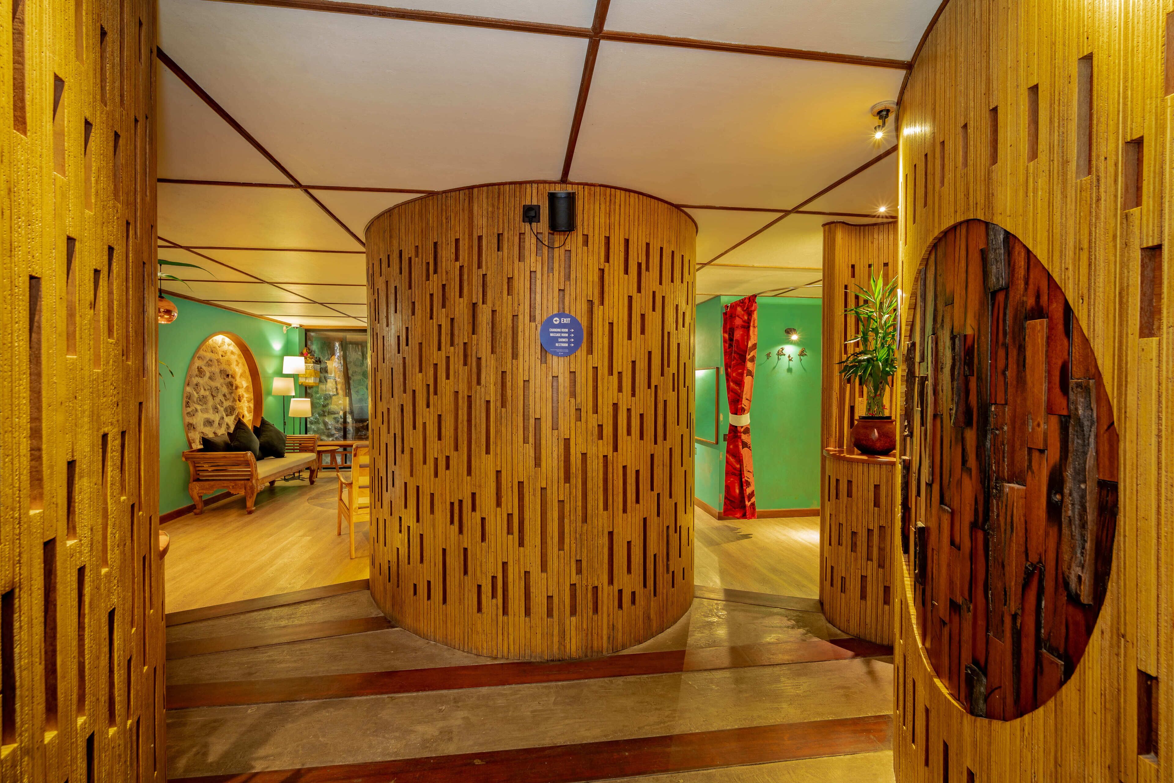 A wooden reception desk with a blue sign, a bench, and a potted plant in a lobby with wooden walls and a green accent wall.