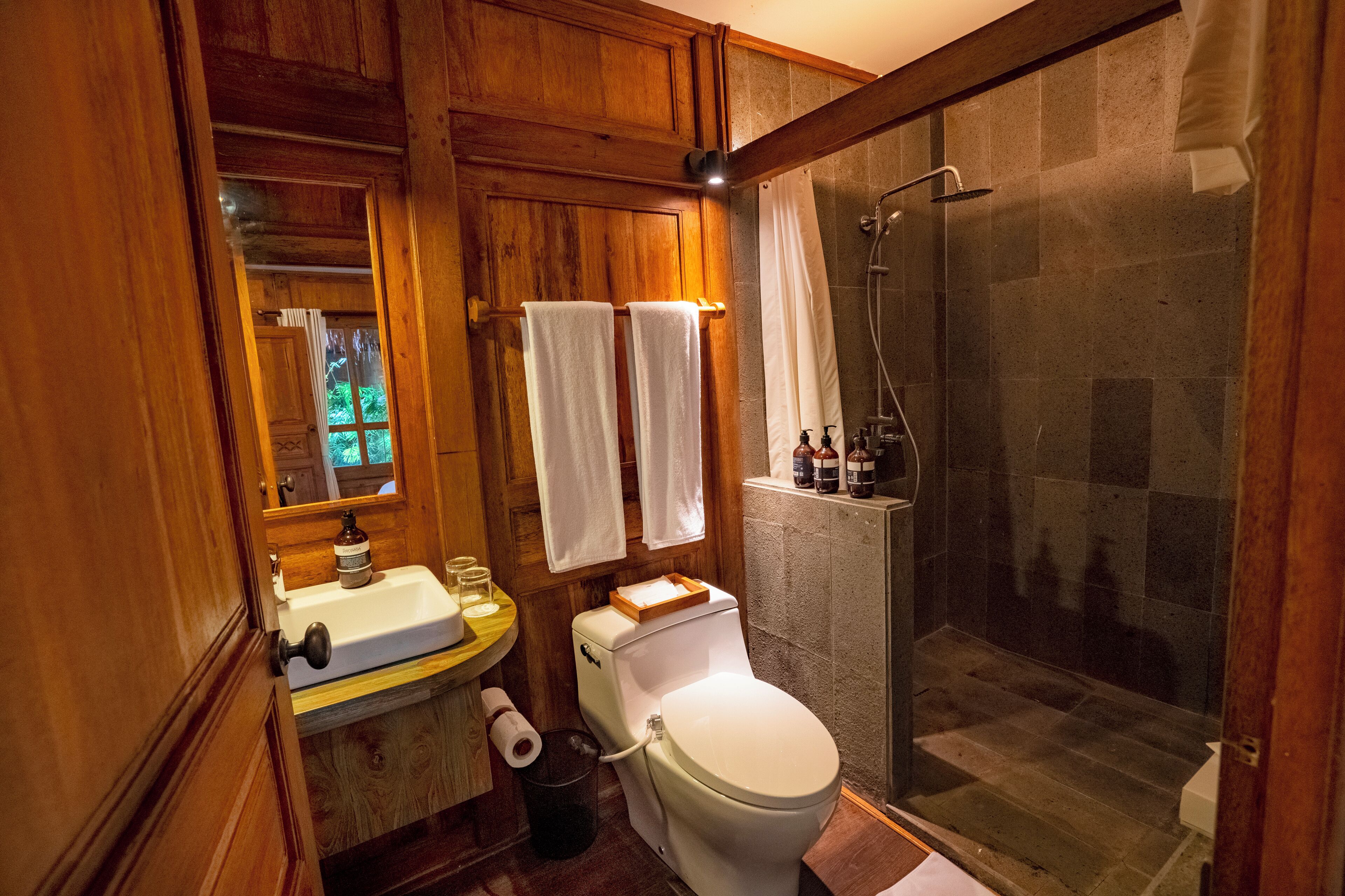 A wooden bathroom with a toilet, sink, and shower.