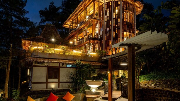A two-story building with a thatched roof, a fire pit, and outdoor seating. - TIRA VILAGNA SUITES & SPA (Kintamani)