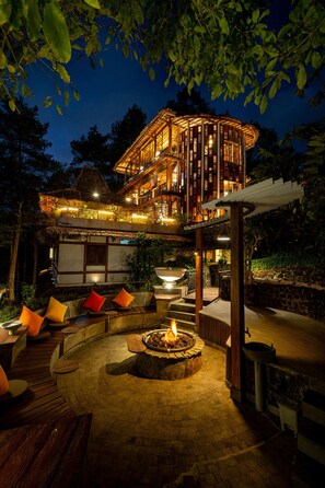 A two-story building with a thatched roof, a fire pit, and outdoor seating. - TIRA VILAGNA SUITES & SPA (Kintamani)