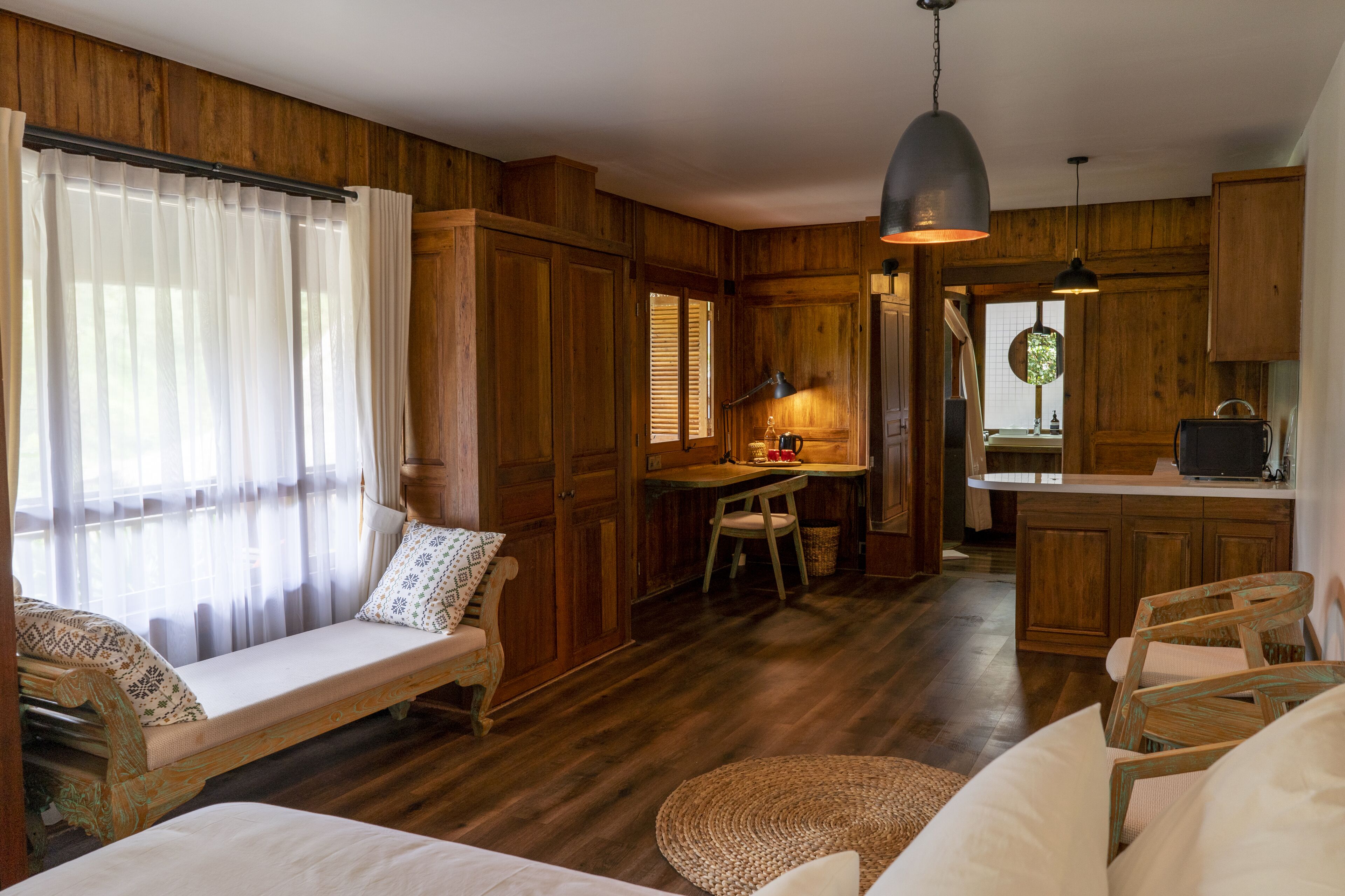 A cozy room with a wooden floor, a sofa, a dining table with chairs, a kitchen area, and a window with curtains.