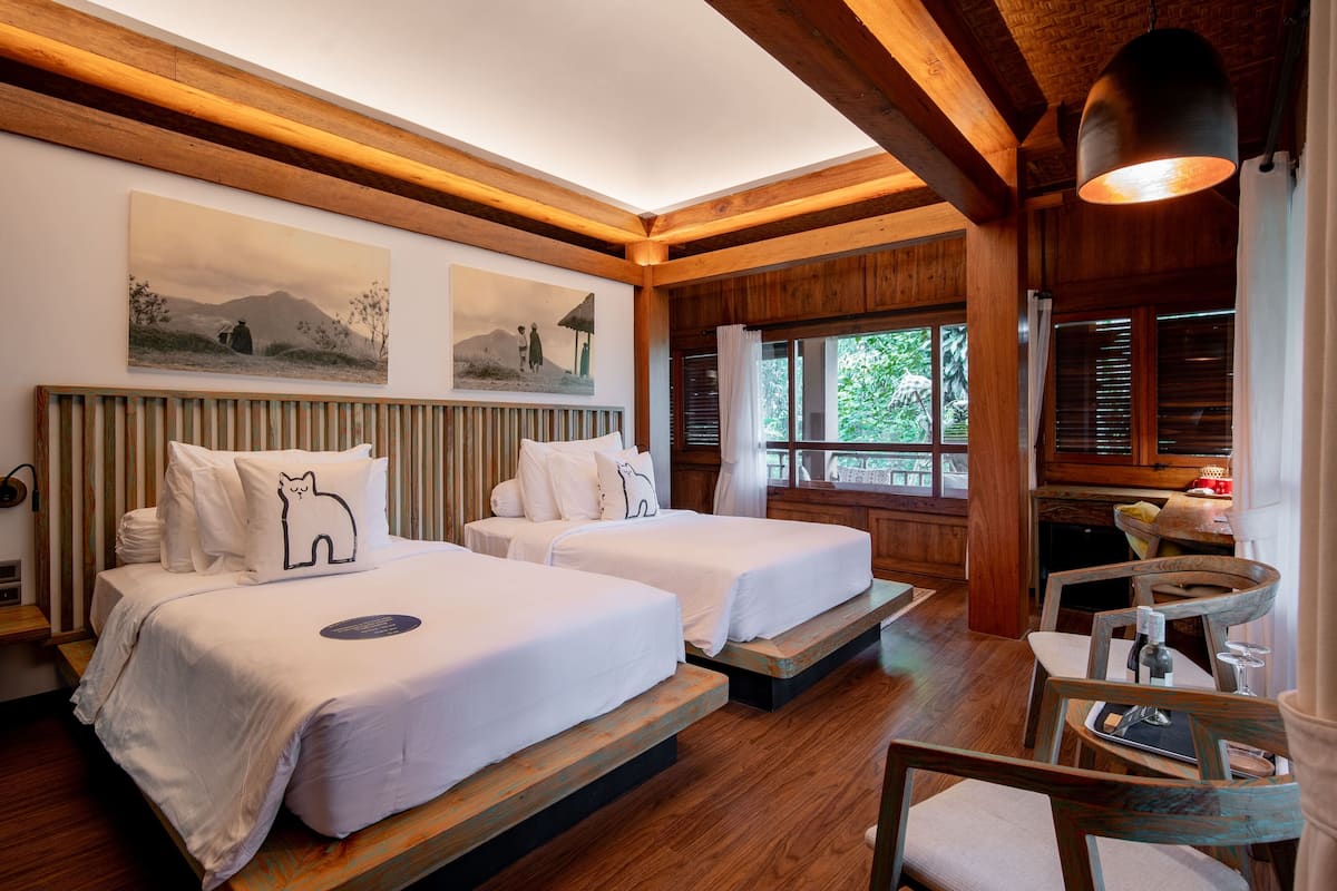 A room with two beds, wooden beams, a dining area, and a view of the outdoors.