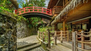 A wooden bridge with a red railing, stone walls, and a thatched-roof building. - TIRA VILAGNA SUITES & SPA (Kintamani)