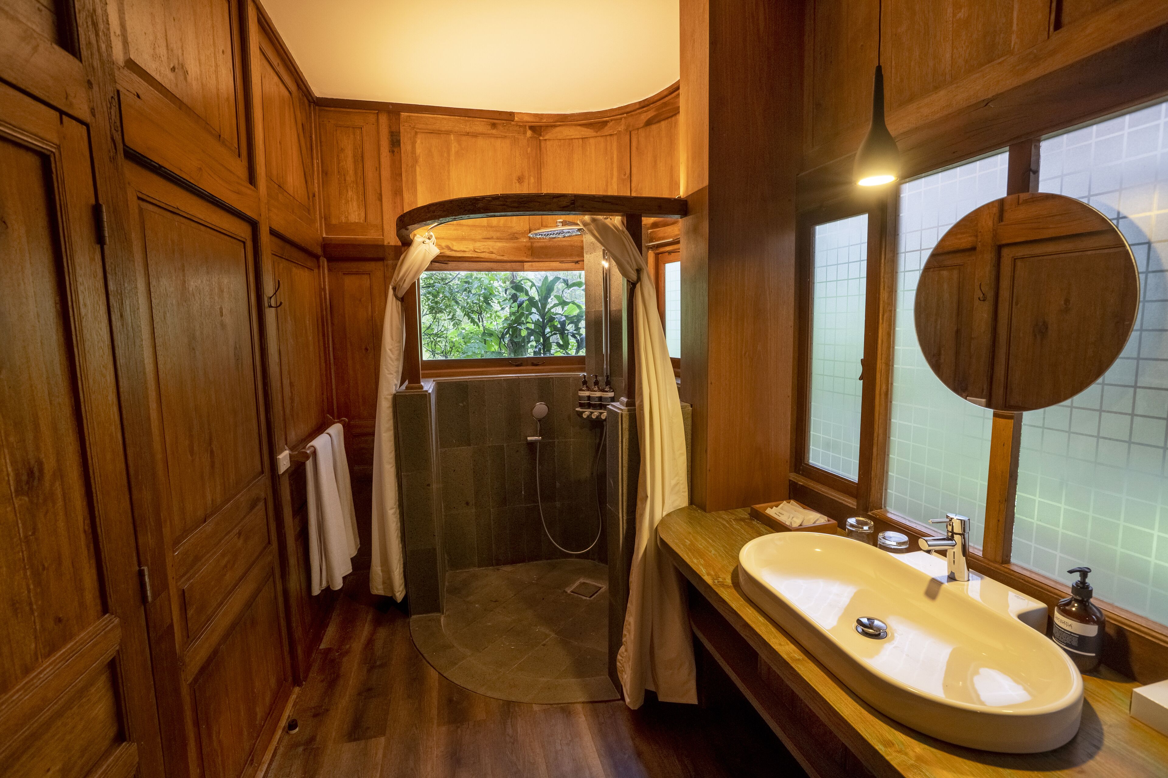 Une salle de bain en bois avec une douche, un lavabo et une fenêtre donnant sur un paysage verdoyant.