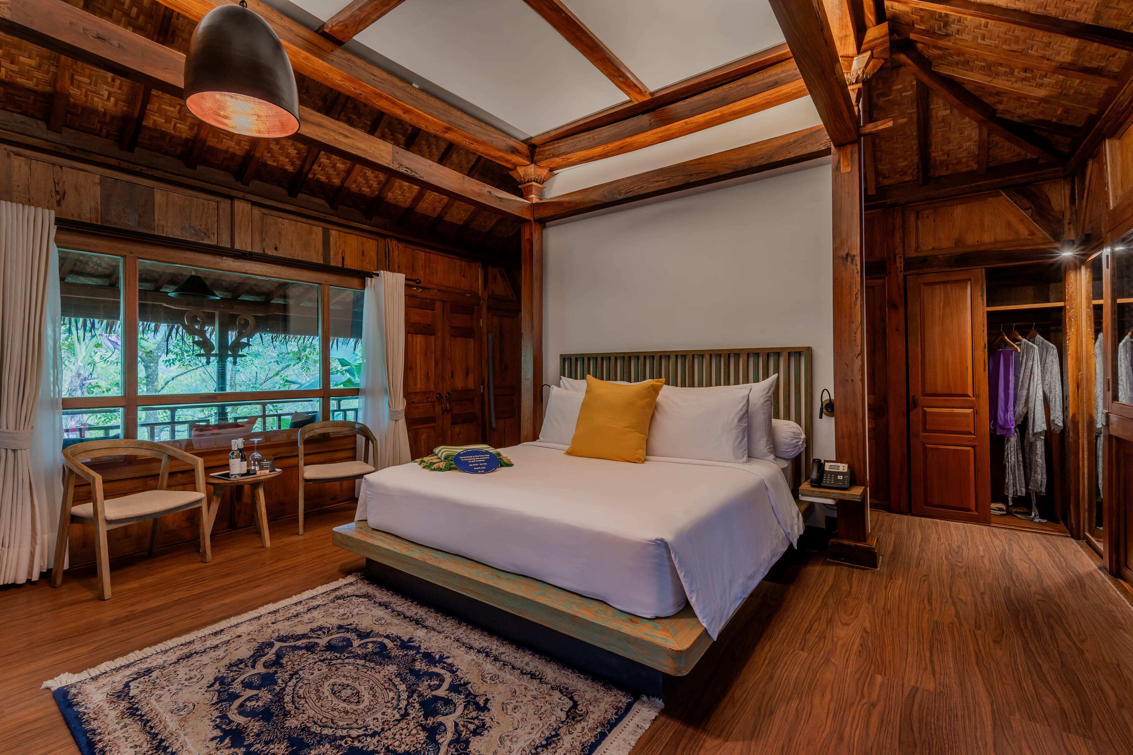 Un dormitorio con una cama grande, muebles de madera, una ventana con cortinas y vistas a árboles.