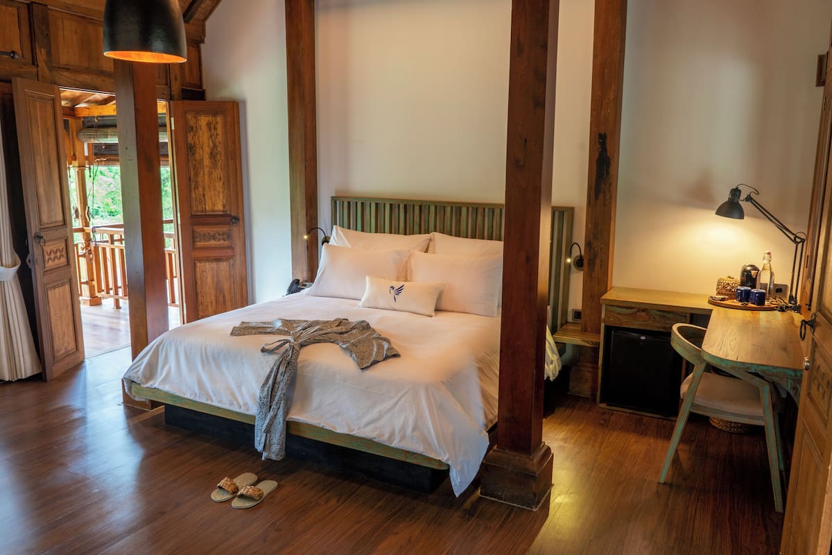 A wooden-framed bedroom with a bed, bedside table, lamp, and slippers on the floor.