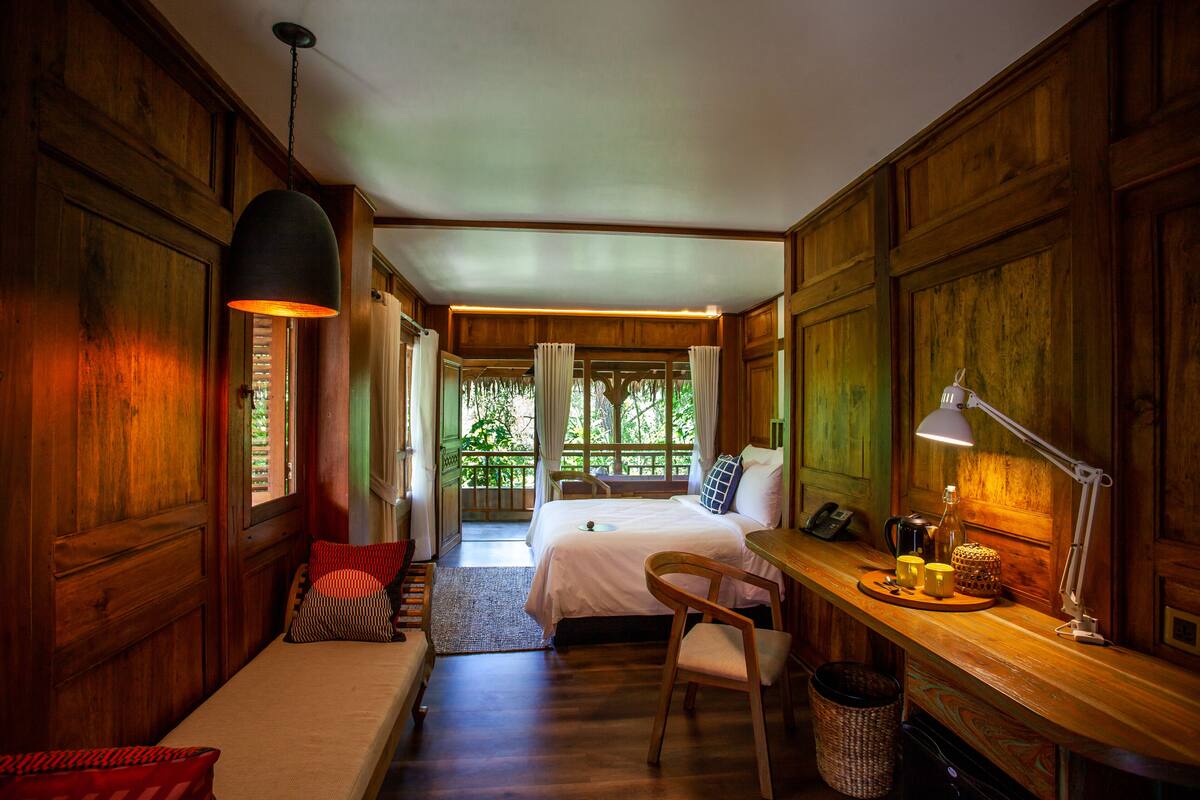 A wooden room with a bed, desk, chair, and a hanging lamp.