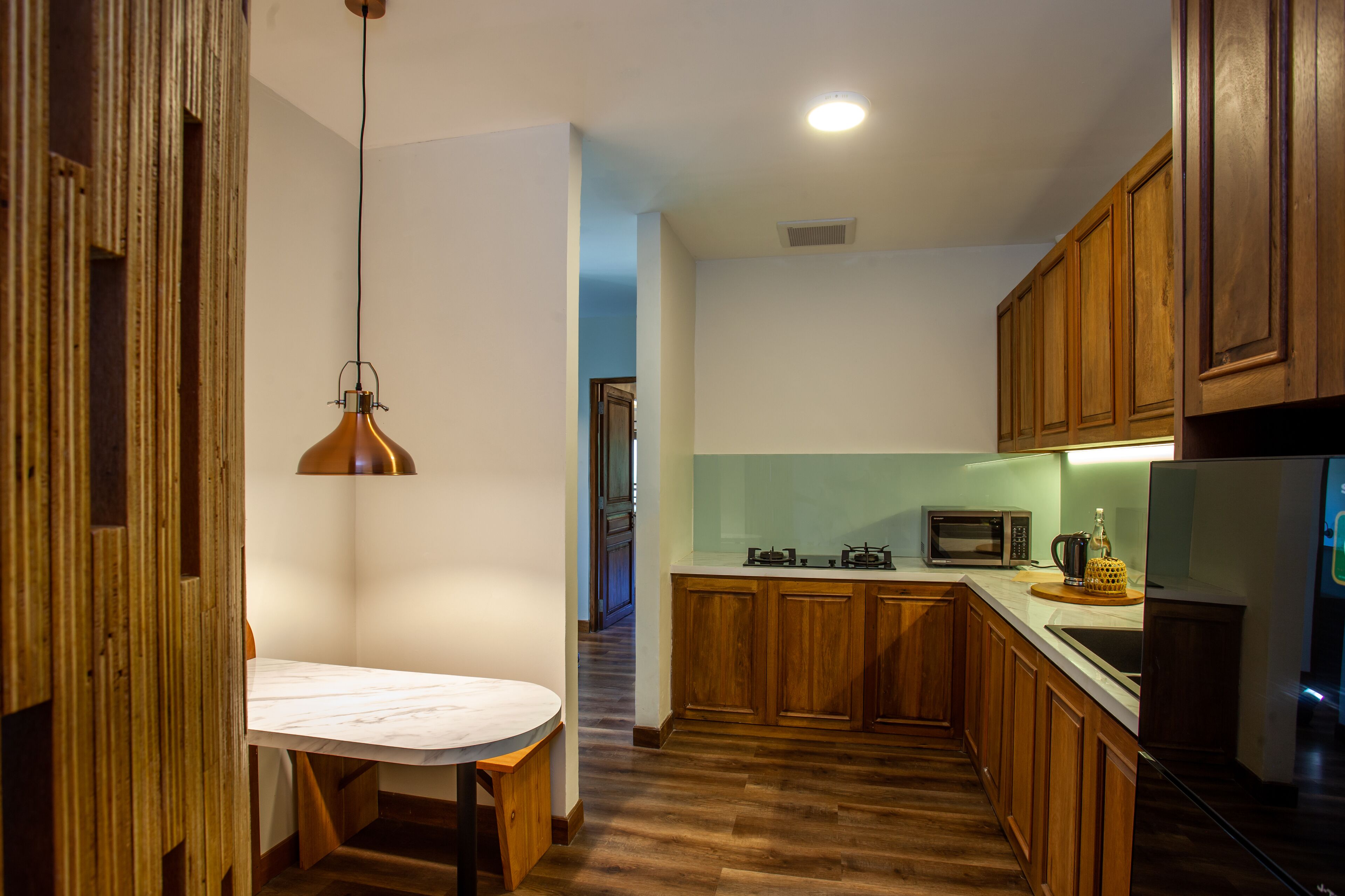 Une cuisine avec des meubles en bois, un plan de travail en marbre, un luminaire suspendu et un four à micro-ondes.