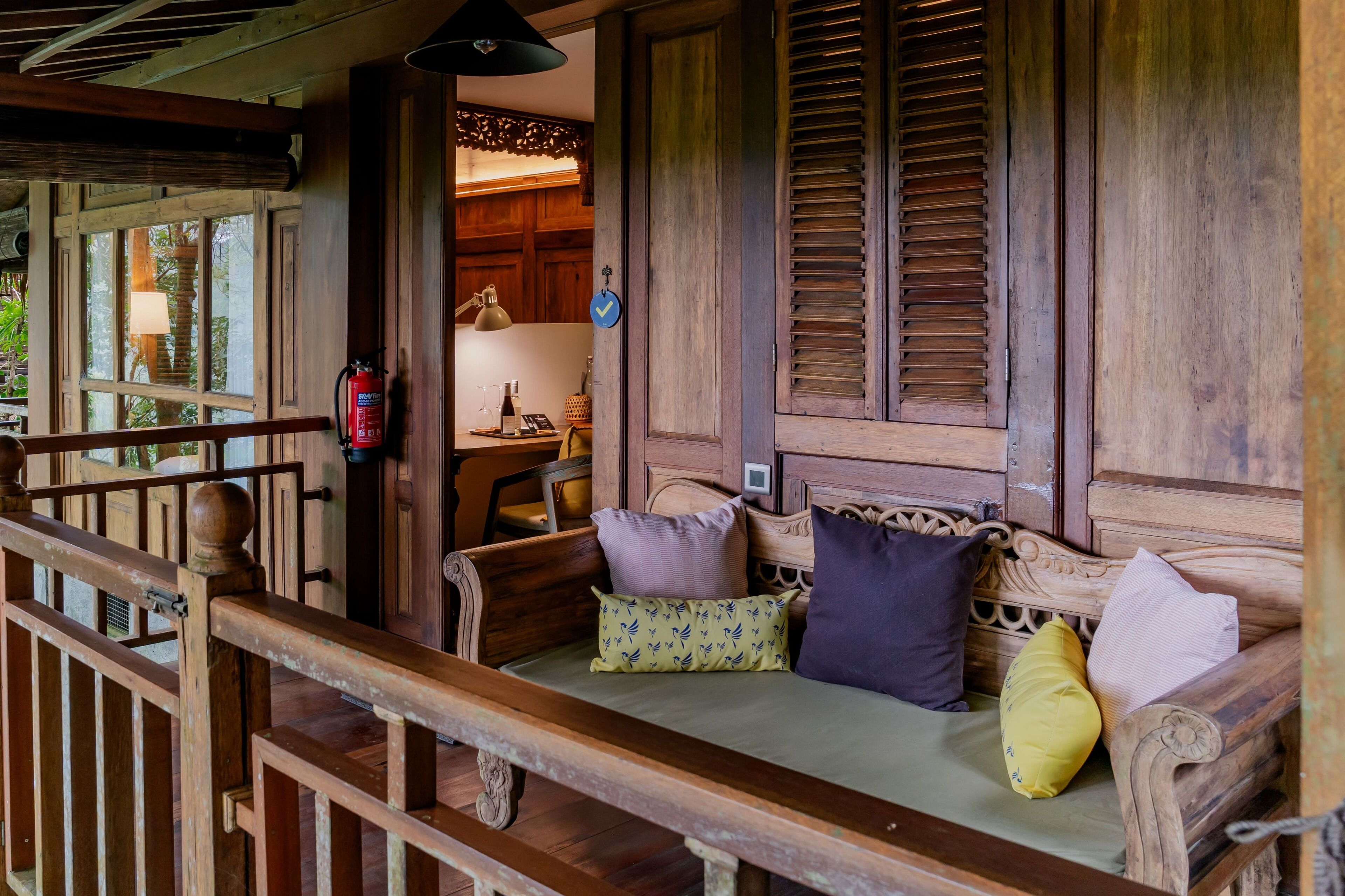 A wooden porch with a bench, a fire extinguisher, and a view of the interior.