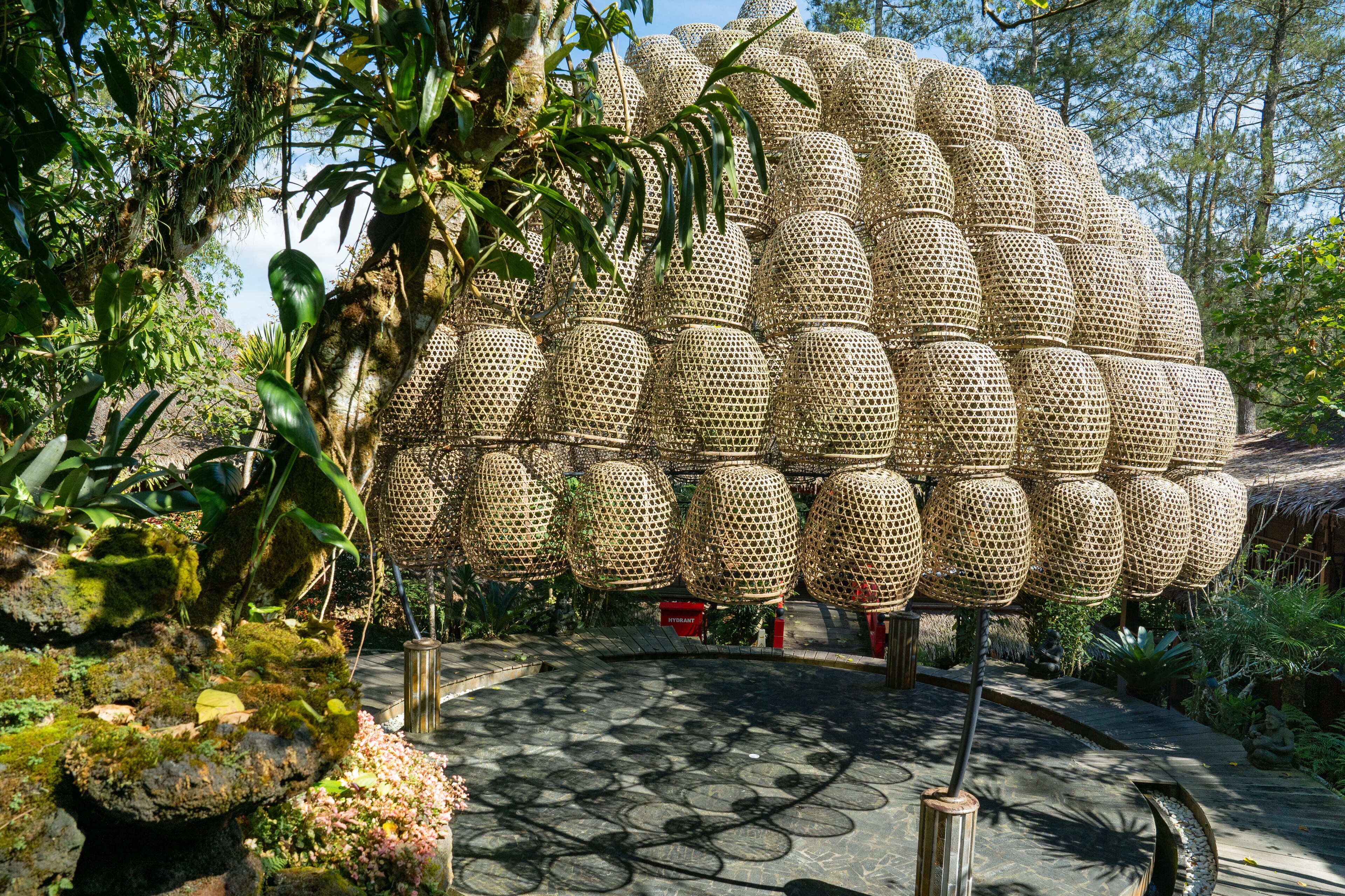 Una gran estructura esférica hecha de material trenzado, rodeada de exuberante vegetación y un sendero de piedra.