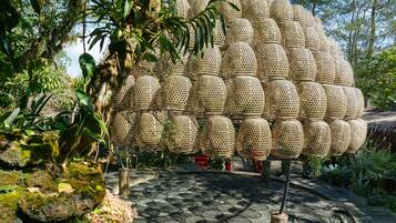 Una gran estructura esférica hecha de material trenzado, rodeada de exuberante vegetación y un sendero de piedra.