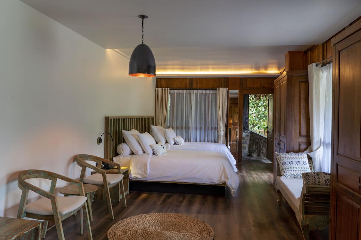 A bedroom with a large bed, a wooden chair, a small table, and a hanging light fixture.