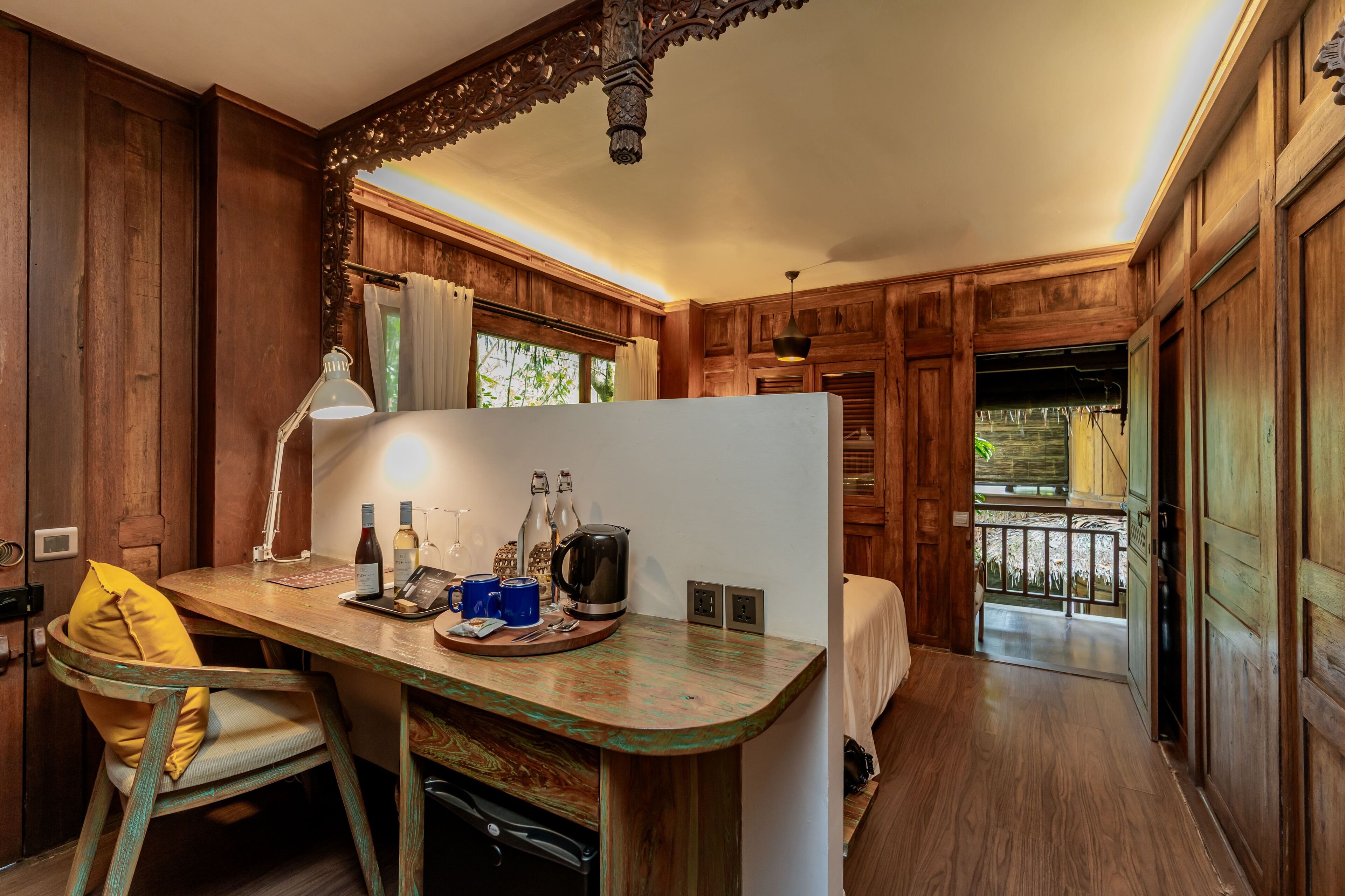 A wooden cabin-style room with a wooden desk, a chair, a bed, and a balcony.