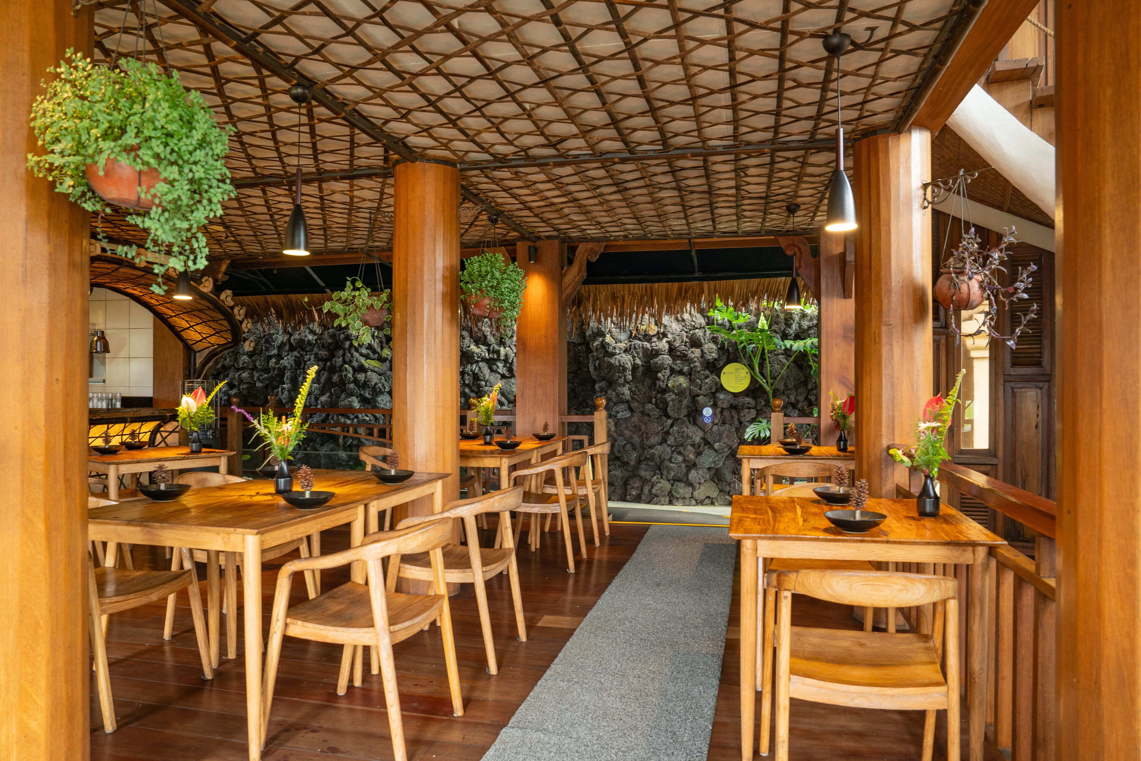 A restaurant with wooden tables and chairs, hanging plants, and a stone wall.