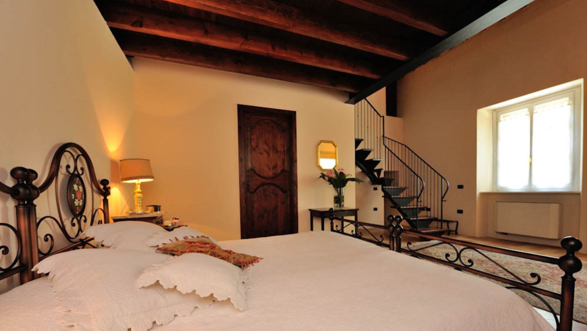 A bedroom with a large bed, a wooden door, a staircase, and a window.