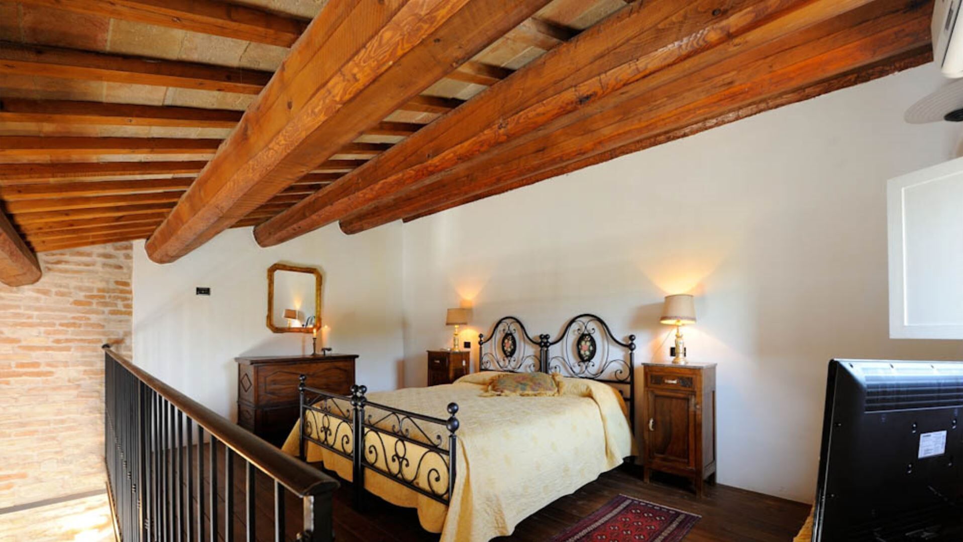 A bedroom with a wooden ceiling, a bed with a headboard, bedside tables with lamps, and a dresser.