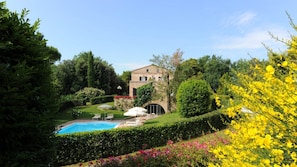 Ein Pool, umgeben von üppiger Vegetation und einem gepflegten Garten, mit einem großen Haus im Hintergrund.