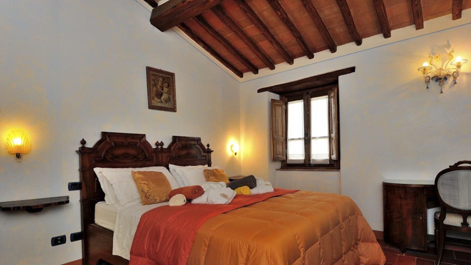 Ein Schlafzimmer mit einem hölzernen Bett, einem Nachttisch, einem Sessel, einem Fenster und Wandleuchten.