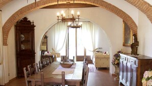 Ein Esszimmer mit einem langen Holztisch, Stühlen, einer Kronleuchter und einem Ziegelbogen.