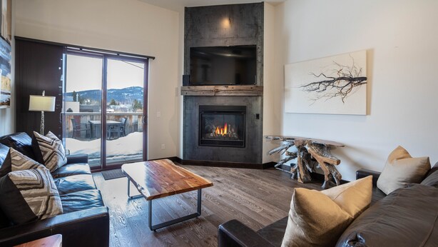Una sala de estar moderna con chimenea, sofás de cuero, una mesa de centro de madera y vistas a través de puertas de cristal grandes.