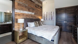 Un dormitorio moderno con una pared de acento de madera, una cama grande, una mesita de noche, un aparador y un armario.