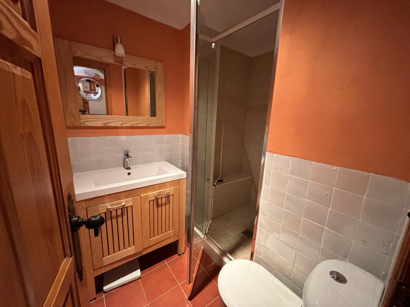 Une salle de bain avec un meuble-lavabo en bois, un lavabo blanc, un miroir, un espace douche et des toilettes.