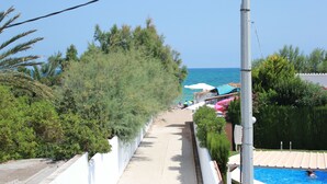 A pathway leading to a pool area with a view of the sea, surrounded by greenery and white walls. - 117 Las Velas, 57 (Denia)