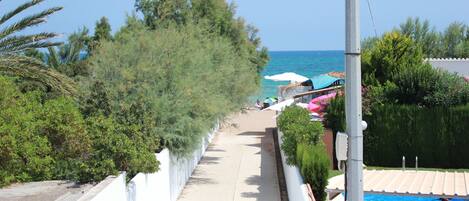 A pathway leading to a pool area with a view of the sea, surrounded by greenery and white walls.