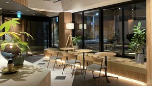 A modern interior with a seating area featuring round tables and chairs, a large potted plant, and a floor lamp. - R Hotel Namba (Osaka)