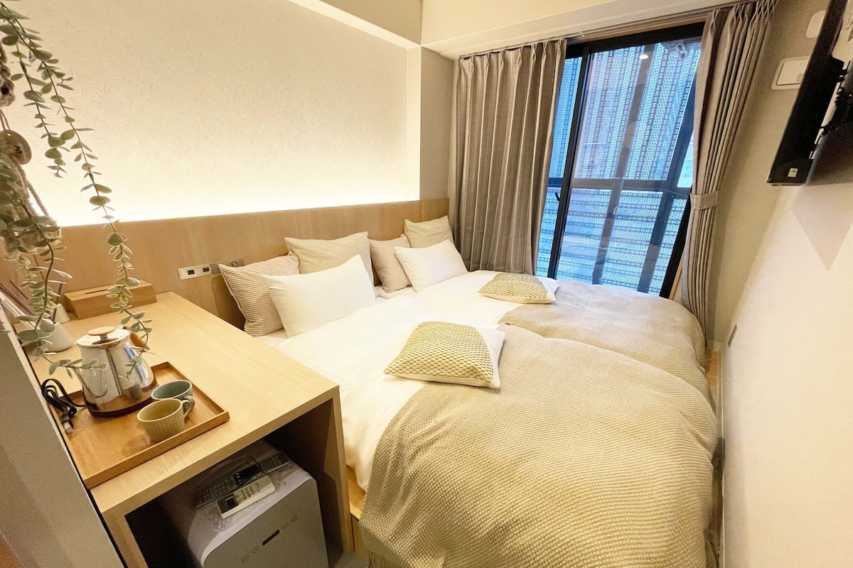 A hotel room with a bed, bedside table, and a window with curtains.