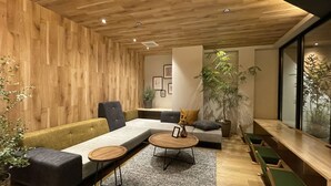 A modern living room with wooden paneling, a sofa, two round coffee tables, and a large plant. - R Hotel Namba (Osaka)