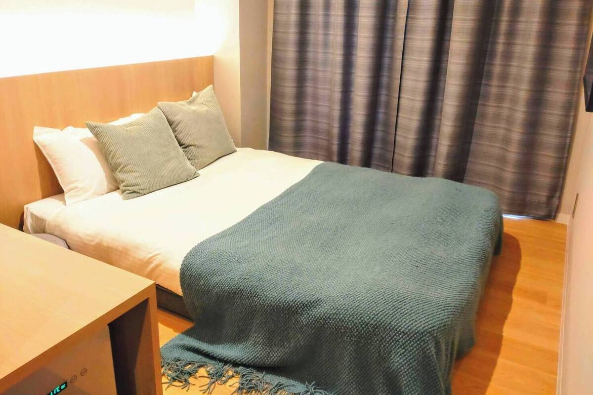 A hotel room with a bed, a wooden headboard, a bedside table, and a curtain.