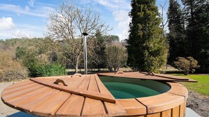A wooden hot tub with a curved edge, surrounded by a landscaped garden with trees and shrubs. - Ecolodge in Remouchamps with sauna (Remouchamps)